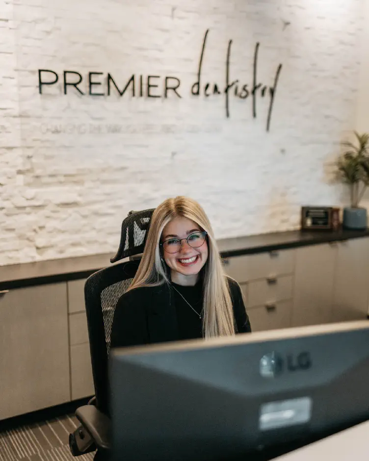 Front desk coordinator smiling at the Premier Dentistry reception desk in Gresham, OR