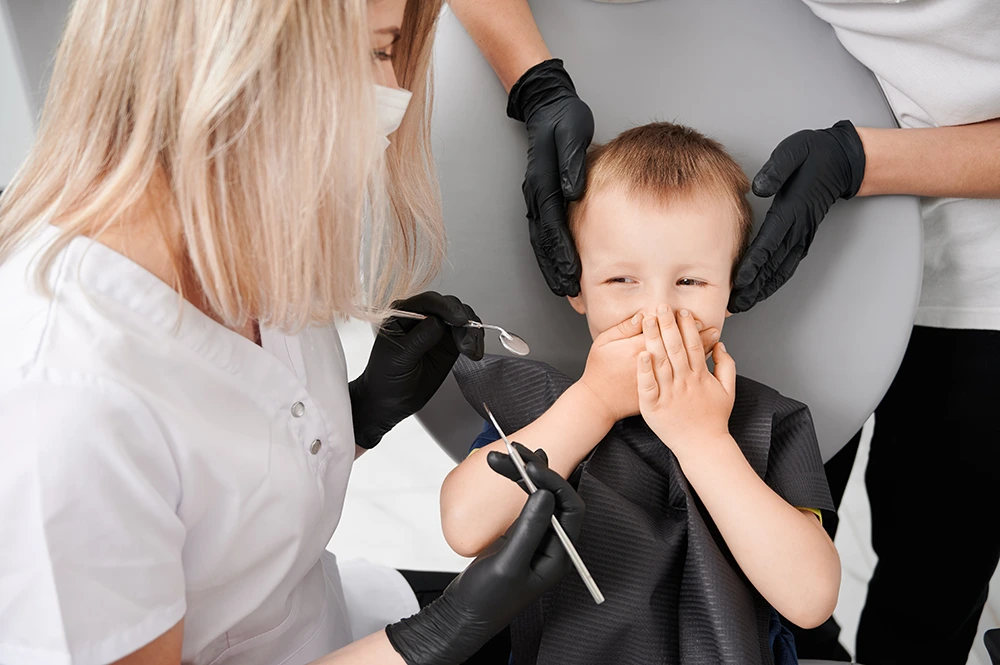 Dental hygienist with a child covering his mouth.